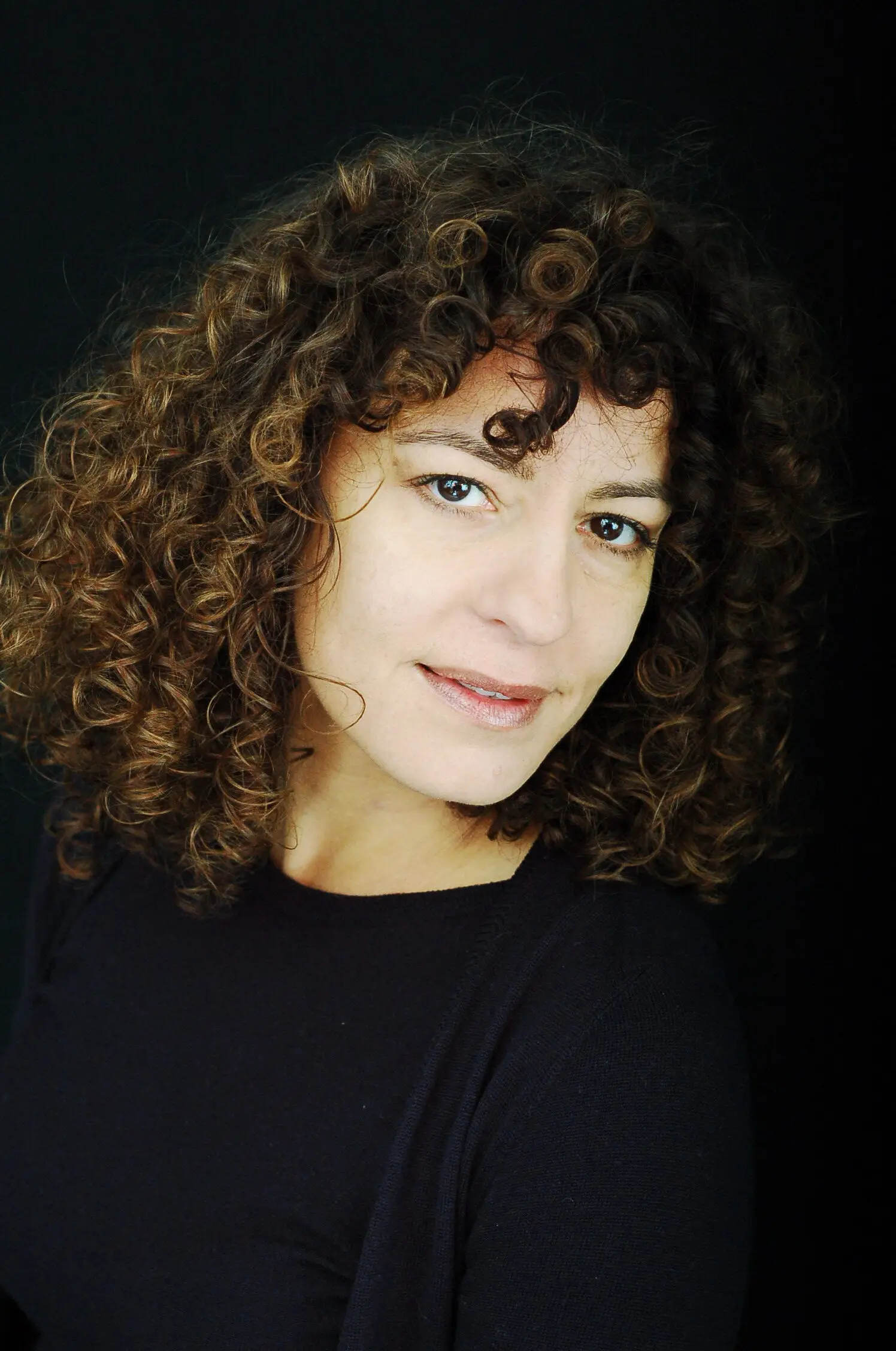 Cristina Monti, operatrice olistica, sorride con i capelli ricci su fondo scuro
